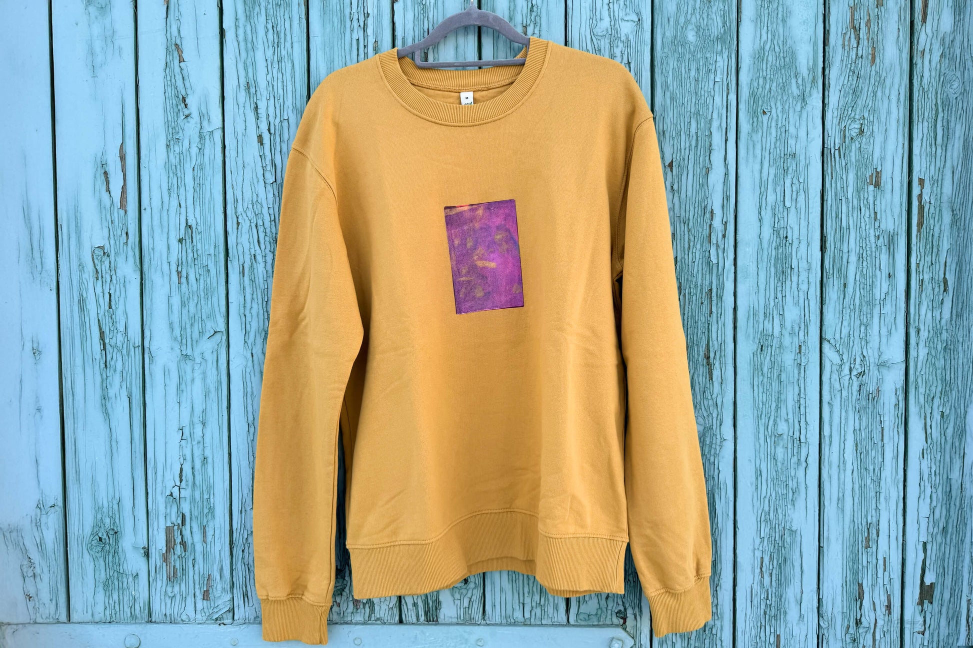 Frontansicht von senffarbenem senffarbenes Unisex Sweatshirt mit lila-gelb verlaufendem Druck von einem großen Rechteck auf der Brust, bedruckt mit Siebdruck. Siebdruck von Jeff EveryPieceAFriend.