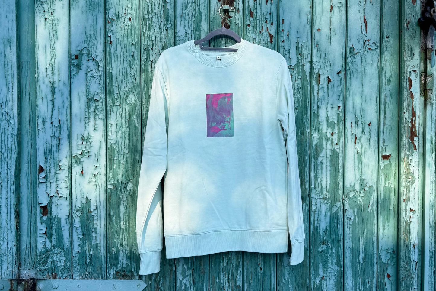 Frontansicht von hellblauen Unisex Sweatshirt mit lila-grün verlaufendem Druck von einem großen Rechteck auf der Brust, bedruckt mit Siebdruck. Siebdruck von Jeff EveryPieceAFriend.