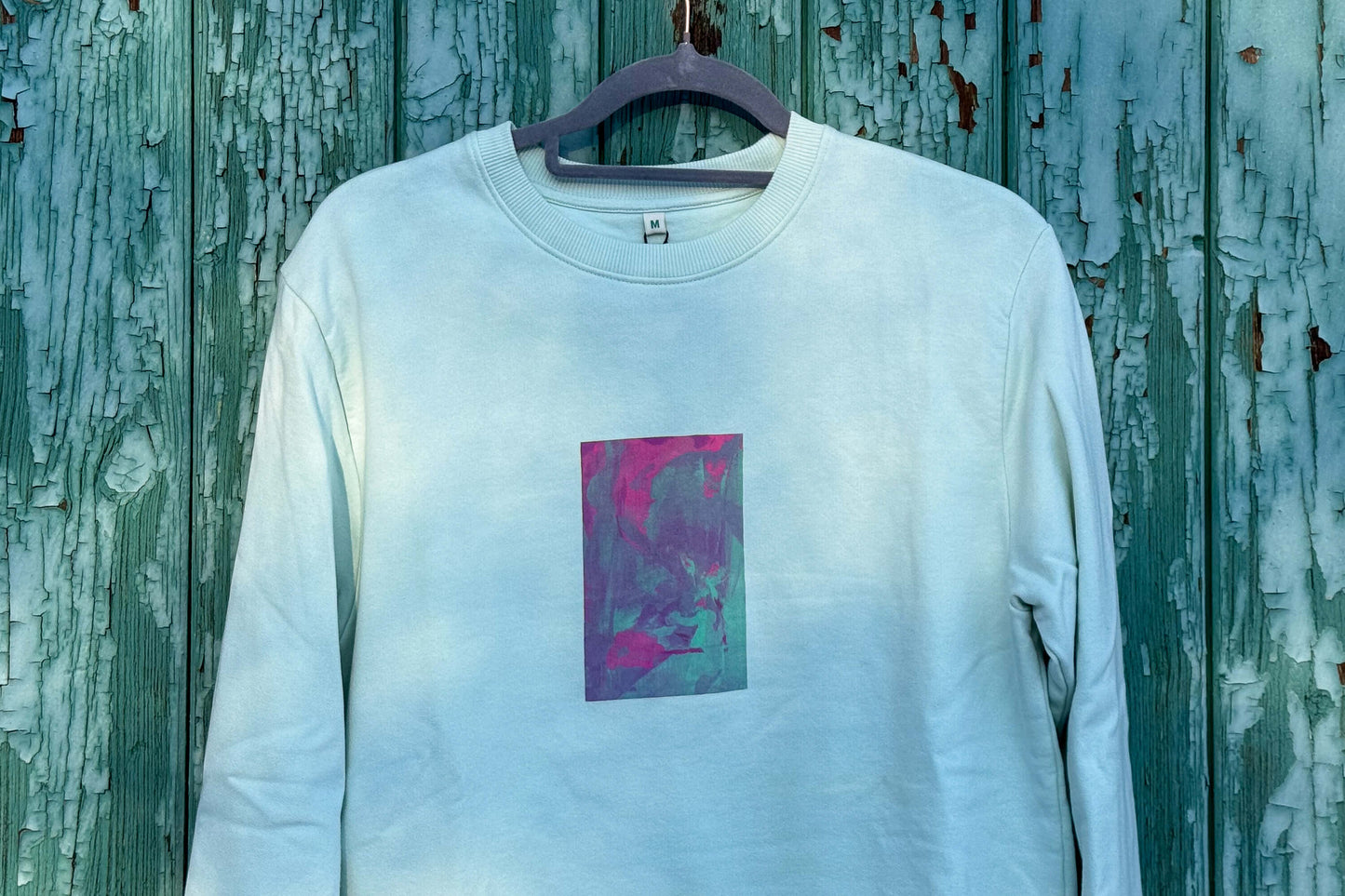 Detailansicht von hellblauen Unisex Sweatshirt mit lila-grün verlaufendem Druck von einem großen Rechteck auf der Brust, bedruckt mit Siebdruck. Siebdruck von Jeff EveryPieceAFriend.