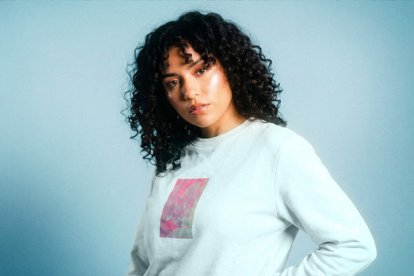 Detailanischt: eine junger Frau trägt ein hellblaues Unisex Sweatshirt mit lila-grün verlaufendem Druck von einem großen Rechteck auf der Brust, bedruckt mit Siebdruck. Siebdruck von Jeff EveryPieceAFriend.