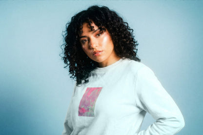 Detailanischt: eine junger Frau trägt ein hellblaues Unisex Sweatshirt mit lila-grün verlaufendem Druck von einem großen Rechteck auf der Brust, bedruckt mit Siebdruck. Siebdruck von Jeff EveryPieceAFriend.