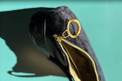 Detailansicht von oben: Schultertasche im Vintagestil vor blau-grauem Hintergrund. Die Tasche ist schwarz gemustert und aus Samt und hat einen goldenen Reißverschluss. Die Tasche wurde aus upcycled Materialien von Jeff Every Piece A Friend hergestellt