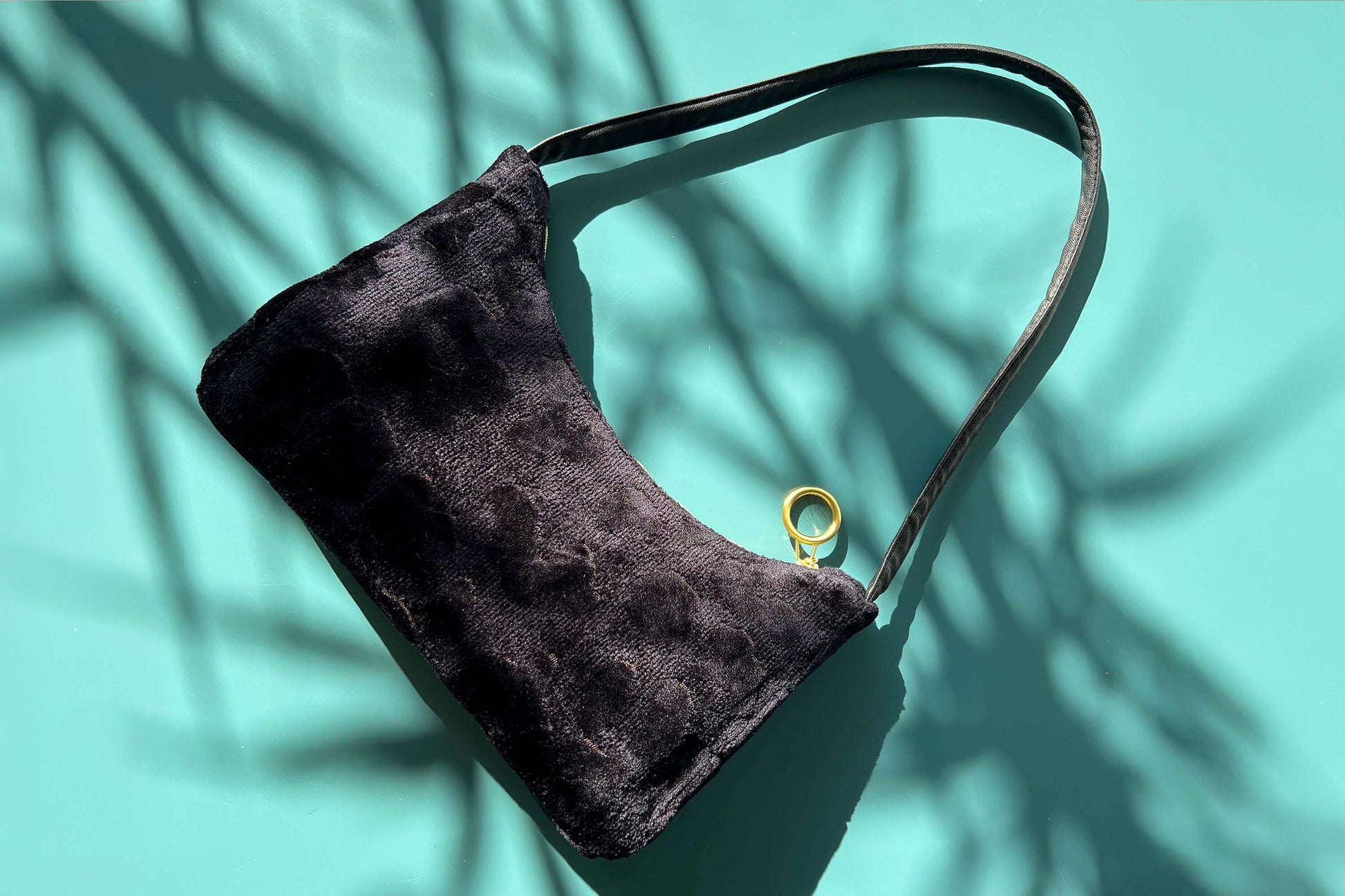 Gesamtansicht: Schultertasche im Vintagestil vor blau-grauem Hintergrund. Die Tasche ist schwarz gemustert und aus Samt und hat einen goldenen Reißverschluss. Die Tasche wurde aus upcycled Materialien von Jeff Every Piece A Friend hergestellt