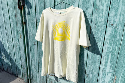 Detailansicht von einem hellgelben T-Shirt in der Größe XL vor einem blauen Hintergrund. Das T-Shirt hat einen welligen, neongelben Druck auf der Brust. Handbedruckt von Jeff - EveryPieceAFriend