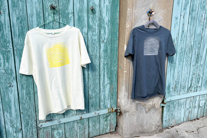 Ansicht von einem grauen und einem hellgelben T-Shirt vor einem blau-beigen Hintergrund. Das graue T-Shirt hat einen welligen Druck in silber, das hellgelbe Shirt einen welligen Druck in gelb auf der Brust. Handbedruckt von Jeff - EveryPieceAFriend