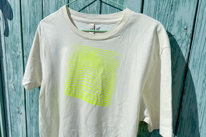 Detailansicht von einem hellgelben T-Shirt vor in der Größe S vor einem blau Hintergrund. Das T-Shirt hat einen welligen, neongelben Druck auf der Brust. Handbedruckt von Jeff - EveryPieceAFriend