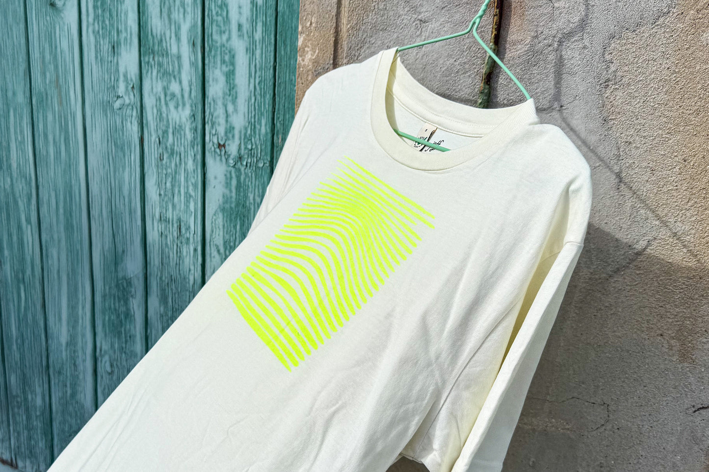 Detailansicht von einem hellgelben T-Shirt vor in der Größe S vor einem blau-beigen Hintergrund. Das T-Shirt hat einen welligen, neongelben Druck auf der Brust. Handbedruckt von Jeff - EveryPieceAFriend