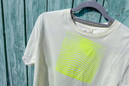 Detailansicht von einem hellgelben T-Shirt in der Größe S vor einem blauen Hintergrund. Das T-Shirt hat einen welligen, neongelben Druck auf der Brust. Handbedruckt von Jeff - EveryPieceAFriend