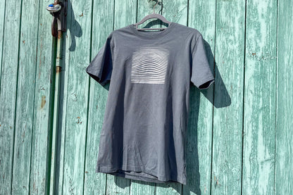 Ansicht von einem grauen T-Shirt in der Größe S vor einem blauen Hintergrund. Das T-Shirt hat einen welligen, silbernen Druck auf der Brust. Handbedruckt von Jeff - EveryPieceAFriend