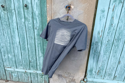 Frontalansicht von einem grauen T-Shirt in Größe S vor einem blau-beige Hintergrund. Das T-Shirt hat einen welligen Druck in silber auf der Brust. Handbedruckt von Jeff - EveryPieceAFriend