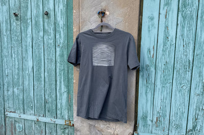 Detailansicht von einem grauen T-Shirt in der Größe S vor einem blau-beigen Hintergrund. Das T-Shirt hat einen welligen, silbernen Druck auf der Brust. Handbedruckt von Jeff - EveryPieceAFriend