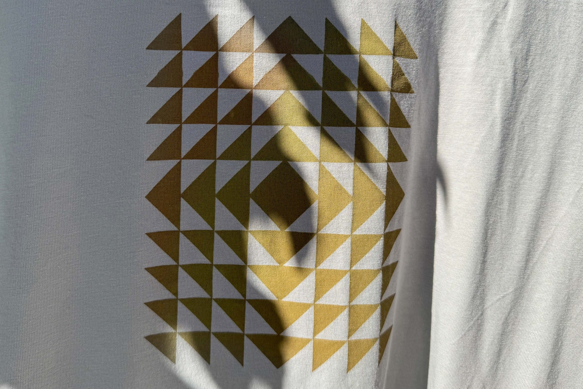 Detailansicht: Vorderseite eines T-Shirt in hellem grau. Das Shirt zeigt ein minimalistisches und geometrisches Muster in der Farbe ocker.