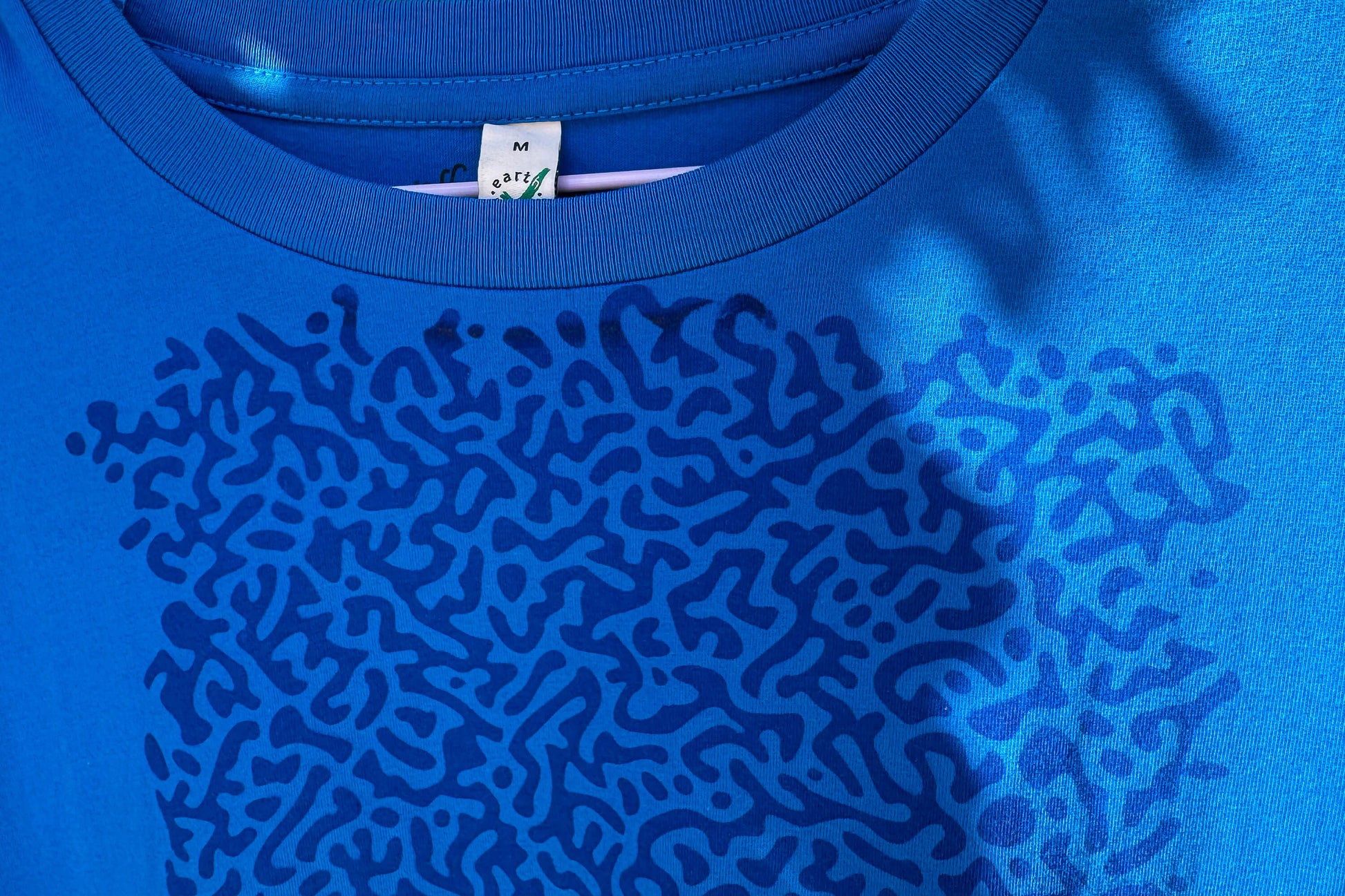 Detailansicht von einem blauen T-Shirt. Das T-Shirt hat einen welligen Druck auf der Brust.