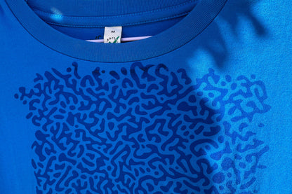 Detailansicht von einem blauen T-Shirt. Das T-Shirt hat einen welligen Druck auf der Brust.