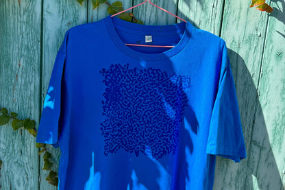 Detailansicht von einem blauen T-Shirt vor einem blauen Hintergrund. Das T-Shirt hat einen welligen Druck auf der Brust.