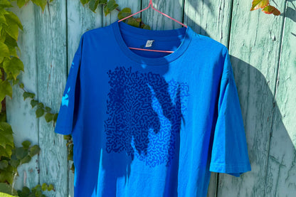 Detailansicht von einem blauen T-Shirt vor einem blauen Hintergrund. Das T-Shirt hat einen welligen Druck auf der Brust.