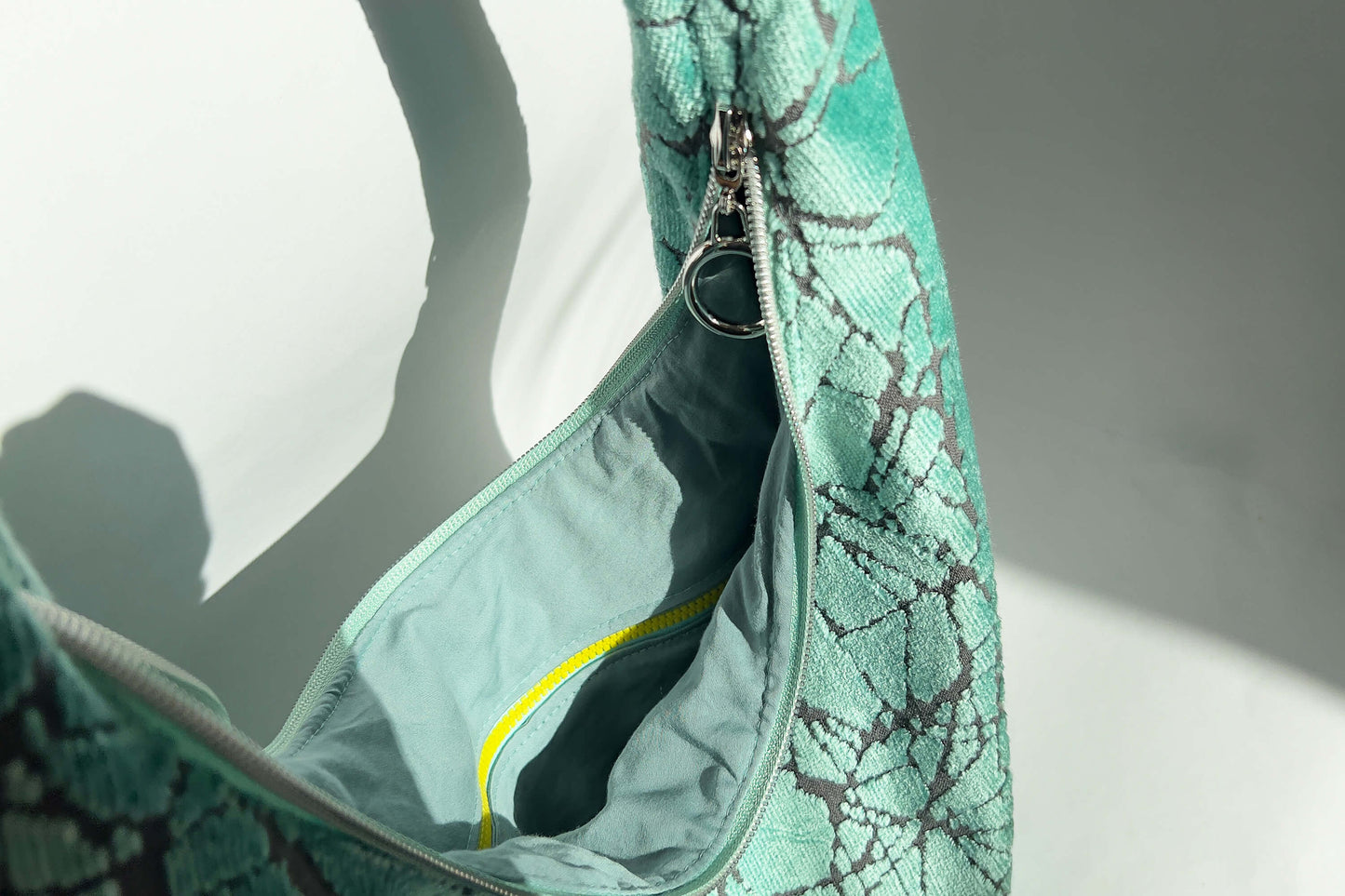 Innenansicht im Detail: Große Crossbody Tasche in hellblauem Muster und silbernen und gelben  Reißverschlüssen steht vor weißem Hintergrund. 