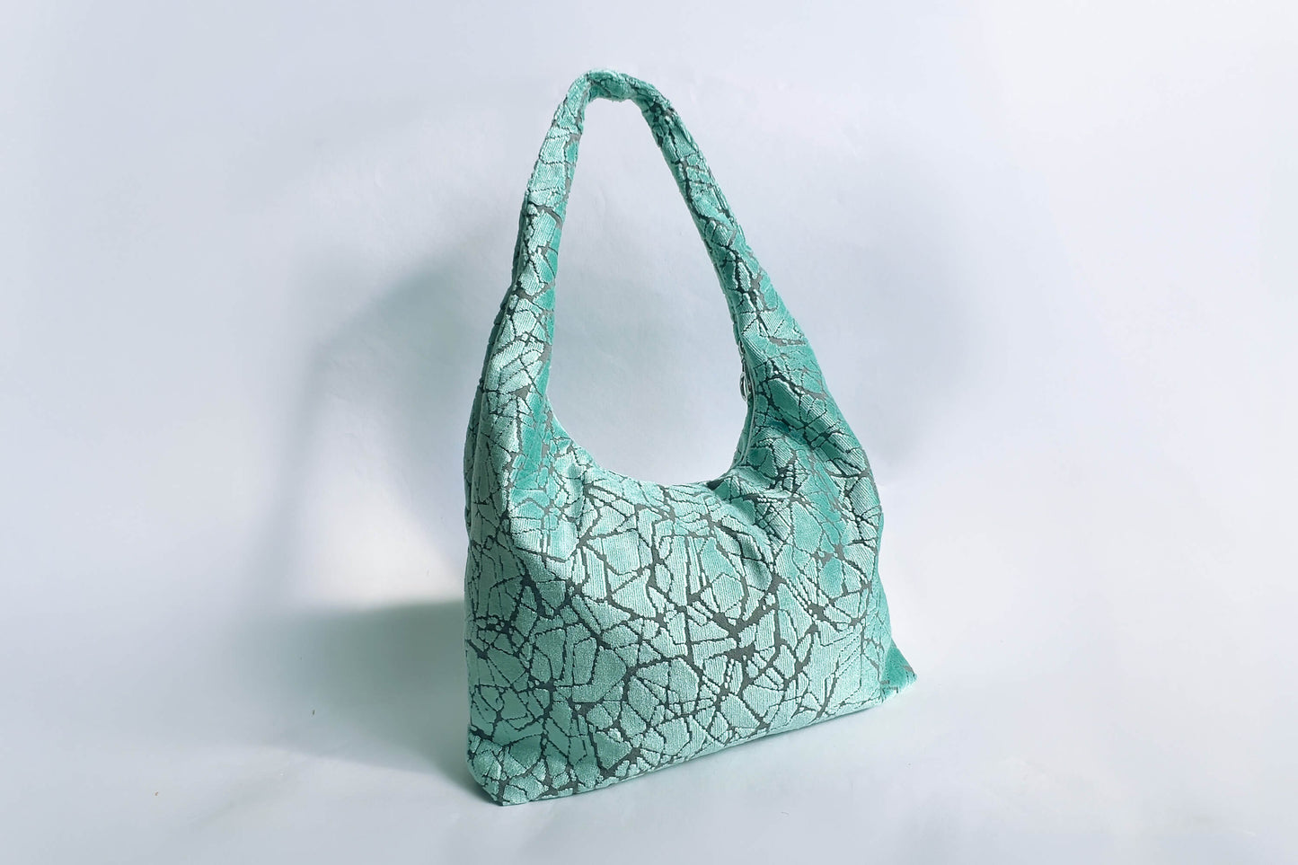 Große Hobo Bag Tasche in hellblauem Muster und silbernen Reißverschluss steht vor weißem Hintergrund. 