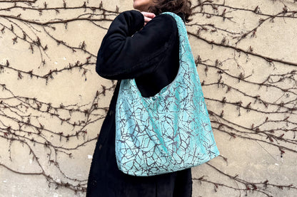 Eine Frau mit schwarzen Mantel und einer hellblauen, großen Hobo Bag, steht seitlich vor einer Wand. 