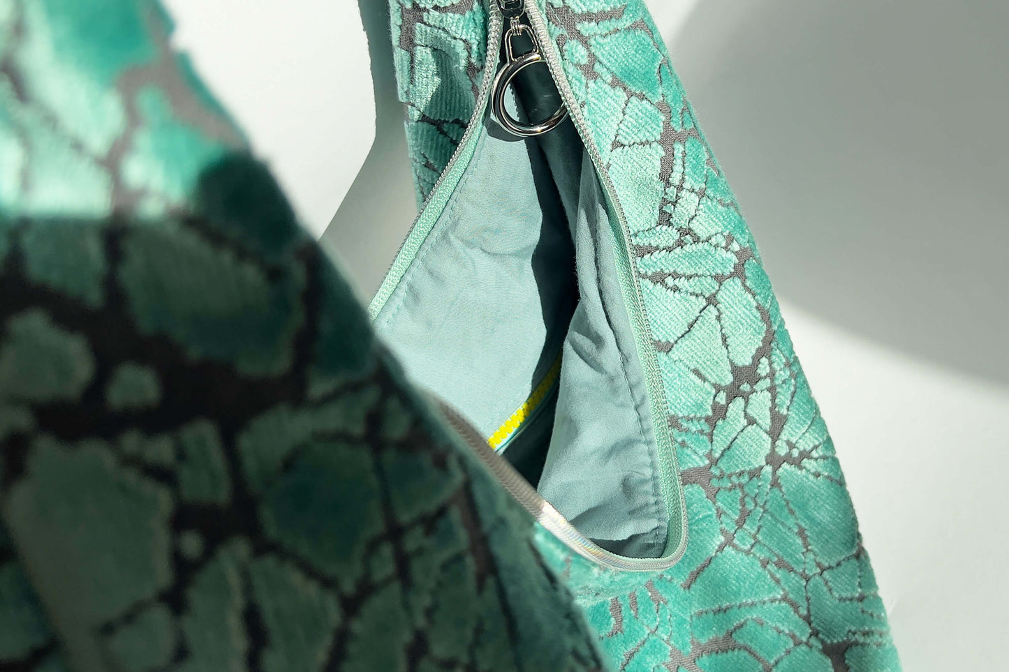 Innenansicht im Detail: Große Crossbody Tasche in hellblauem Muster und silbernen und gelben  Reißverschlüssen steht vor weißem Hintergrund. 