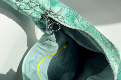 Innenansicht im Detail: Große Crossbody Tasche in hellblauem Muster und silbernen und gelben  Reißverschlüssen steht vor weißem Hintergrund. 