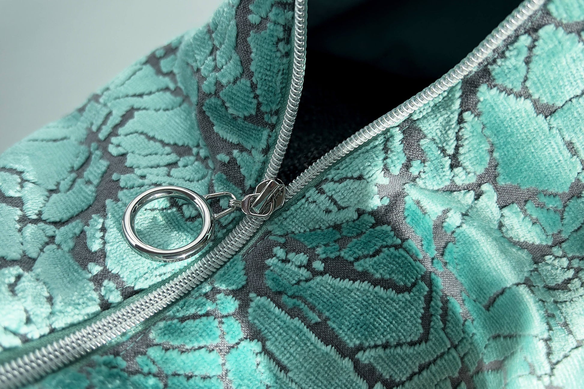 Detailansicht: Große Crossbody Tasche in hellblauem Muster und silbernen Reißverschluss steht vor weißem Hintergrund. 