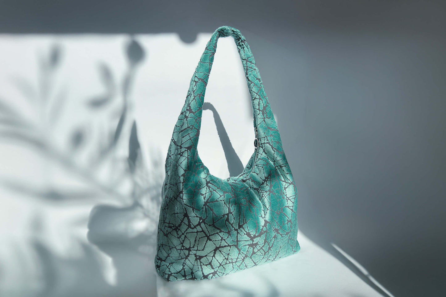 Große Crossbody Tasche in hellblauem Muster und silbernen Reißverschluss steht vor weißem Hintergrund. 