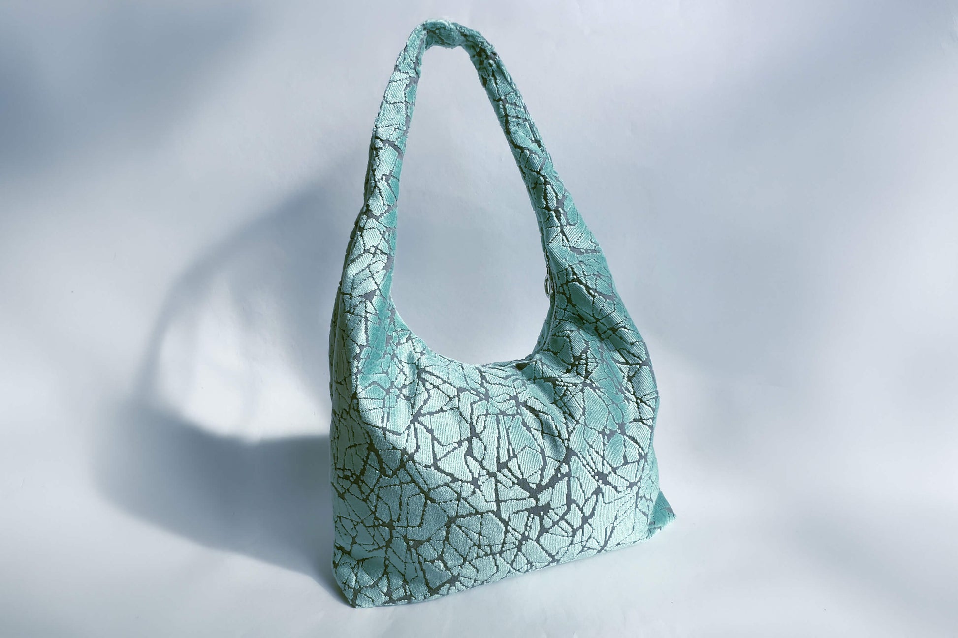 Große Crossbody Tasche in hellblauem Muster und silbernen Reißverschluss steht vor weißem Hintergrund. 