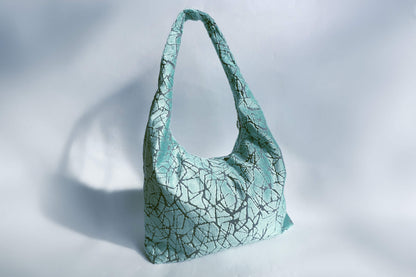 Große Crossbody Tasche in hellblauem Muster und silbernen Reißverschluss steht vor weißem Hintergrund. 