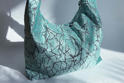 Detailansicht: Große Crossbody Tasche in hellblauem Muster und silbernen Reißverschluss steht vor weißem Hintergrund. 