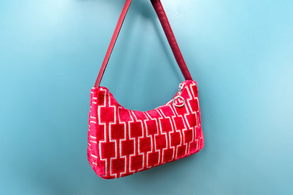 Gesamtansicht: Schultertasche im Vintagestil vor blauen Hintergrund. Die Tasche ist rot gemustert und aus Samt und hat einen silbernen Reißverschluss. Die Tasche wurde aus upcycled Materialien von Jeff Every Piece A Friend hergestellt.