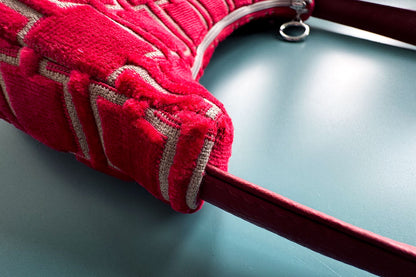 Detailansicht: Schultertasche im Vintagestil vor blauen Hintergrund. Die Tasche ist rot gemustert und aus Samt und hat einen silbernen Reißverschluss. Die Tasche wurde aus upcycled Materialien von Jeff Every Piece A Friend hergestellt.