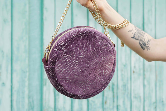 Frau hält rund Umhängetasche VIOLA aus upgecycelten Polsterstoffen mit goldener Kette ins Bild