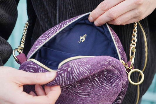 Frau zeigt Innenleben der runden Umhängetasche VIOLA aus upgecycelten Polsterstoffen mit Logo von jeff every piece a friend