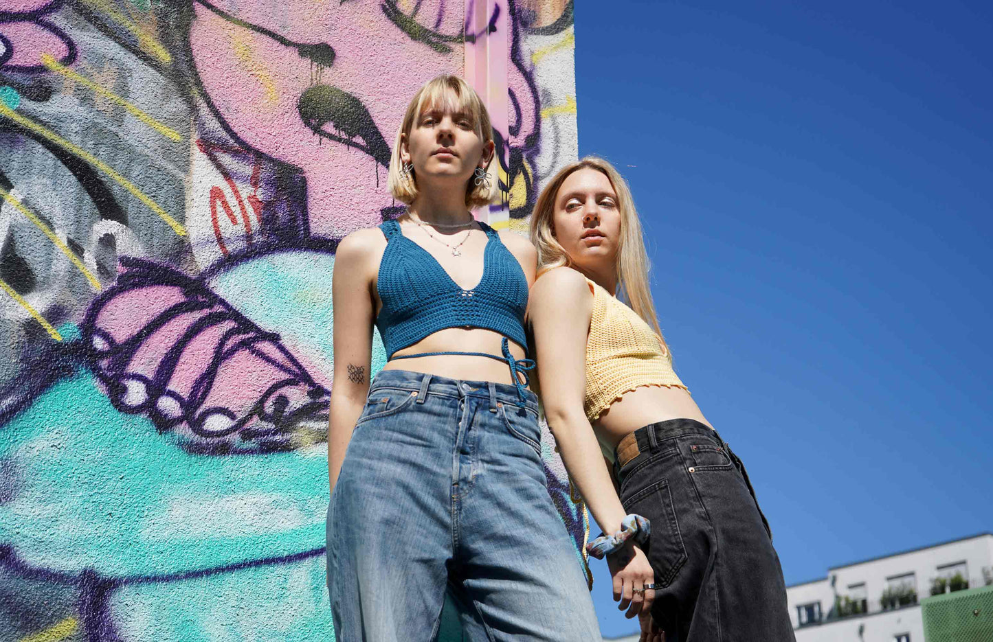 Zwei junge Frauen tragen ein blaues und gelbes Häkeltop YAEL, aus Wolle aus zweiter Hand gehäkelt von jeff every piece a friend