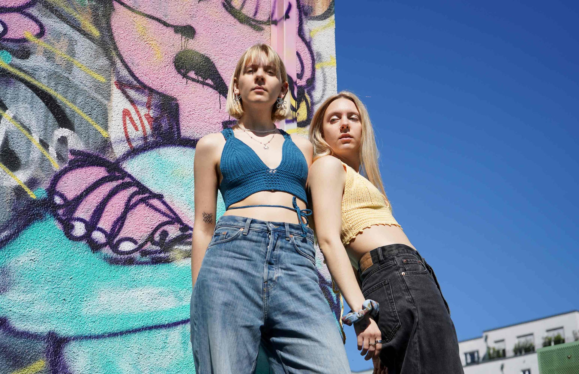 Zwei junge Frauen tragen ein blaues und gelbes Häkeltop YAEL, aus Wolle aus zweiter Hand gehäkelt von jeff every piece a friend