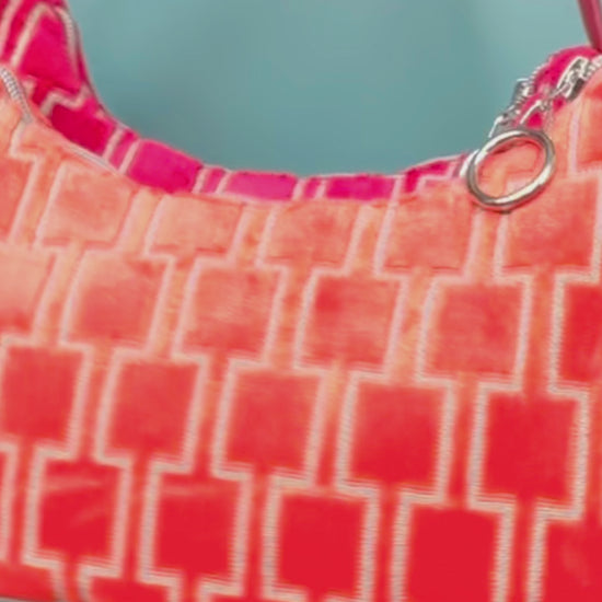 Viedeo Gesamtansicht: Zwei Schultertaschen im Vintagestil vor blauen Hintergrund. Eine Tasche ist orange gemustert, die andere Tasche ist rot gemustert. Beide Taschen wurden von aus upcycled Materialien von Jeff Every Piece A Friend hergestellt.